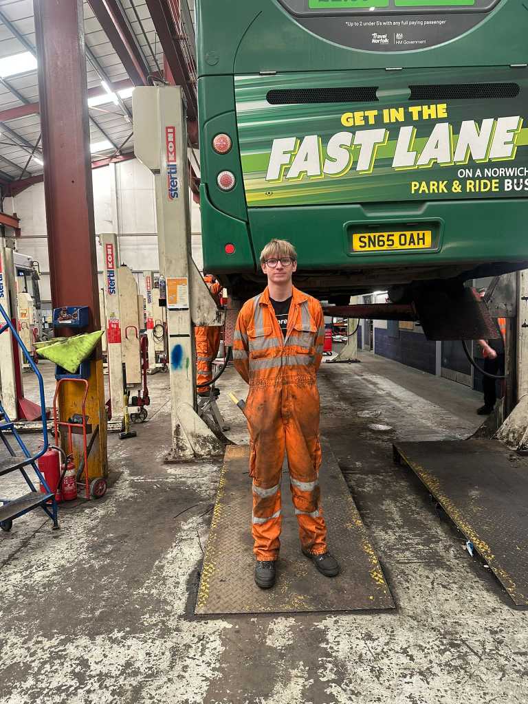 Apprentice Kerian Mottershaw in front of a bus in overalls 